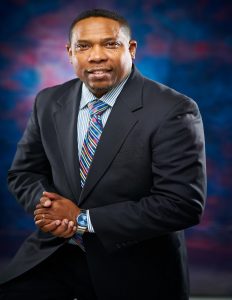 Welcome to Our Church message from Rev. Dr. Cedric L. Perkins standing in a blue suit with his hands clasp with a blue and purple background.